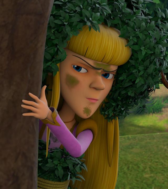 Nelly versteckt sich hinter einem Baum, hält sich mit der linken Hand am Stamm fest und beobachtet kritisch. Ihr Gesicht ist mit grünen Flecken beschmiert und sie trägt zur Tarnung Blätter auf ihrem blonden Haar.