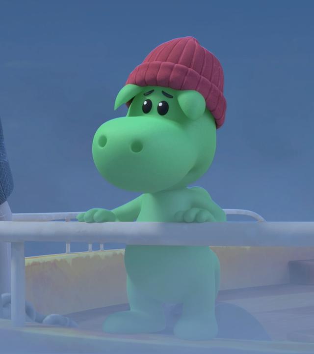 Der grüne Drache Grisu trägt ein pinkfarbenes Strickmützchen. Er steht neben Kapitän Oliver am Bug eines Schiffes. Um sie herum ist dichter Nebel.