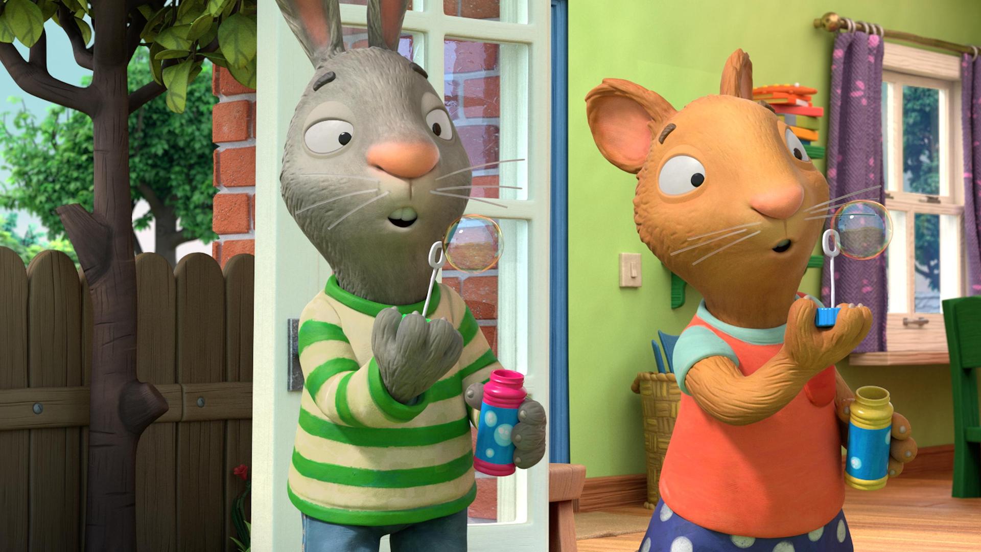 Die beiden allerbesten Freunde Pip das Kaninchen und Posy die Maus stehen draußen vor der geöffneten Terassentür und machen einen Seifenblasen-Wettbewerb. Sie stehen nebeneinander, halten jeweils ein Fläschchen mit Seifenblasenflüssigkeit in ihrer Hand und pusten vorsichtig. Die Seifenblasen der beiden sind fast gleich groß.