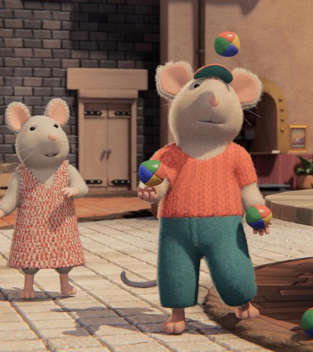 Im Hof des Mäusehauses steht Dan neben dem Brunnen und jongliert mit drei bunten Jonglierbällen Julia steht schräg hinter ihm und schaut ihm bewundernd zu. Sam steht neben Julia und hat die Arme beleidigt vor der Brust verschränkt. Hinter ihnen sieht man die Fassade des Mäusehauses.