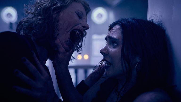 "Love Sucks - Asche zu Asche": Agata (Dana Herfurth) hat ihre Vampirzähne gefletscht und Zelda (Havana Joy) an die Wand gedrängt. Agata ist im Begriff, Zelda am Hals zu beißen. Zelda hält ängstlich und dem Tod ins Auge blickend mit ihrer rechten Hand Agatas Gesicht von sich weg.