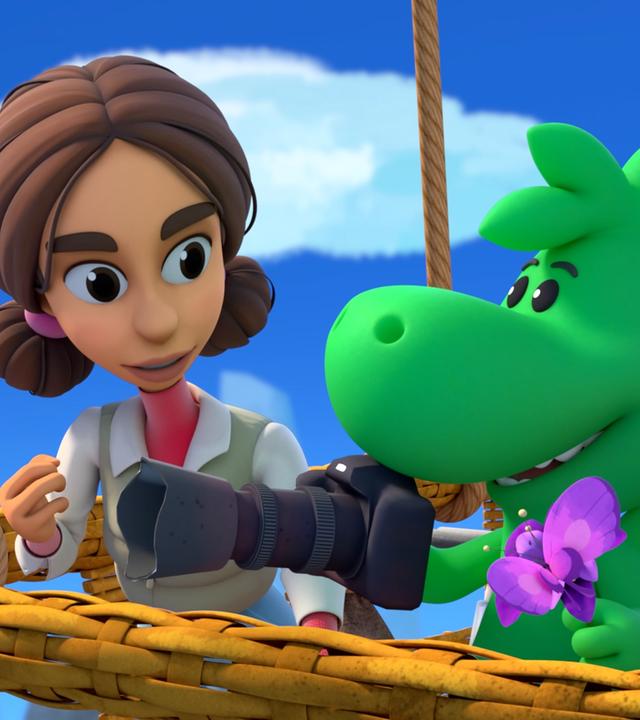 Der kleine Drache Grisu und die Forscherin Natureza stehen im Korb eines Heißluftballons. Grisu trägt in einer Hand eine lilafarbene Blume. Auf dieser sitzt ein lilafarbener Schmetterling. In der anderen Hand hält er eine große Fotokamera. Natureza macht eine entschlossene Geste.