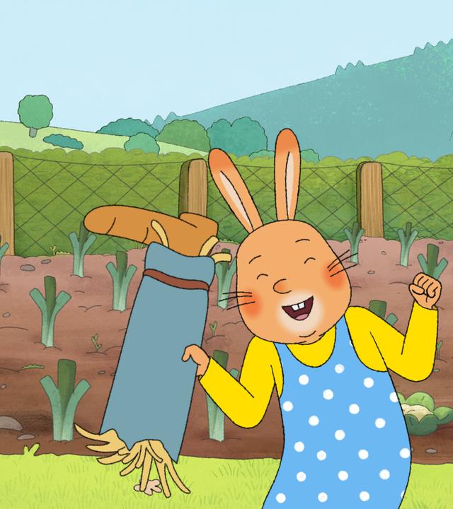 Karlchen und Monika sind im Garten.  Monika hält ein mit Stroh ausgestopftes Hosenbein in der Hand und jubelt. Karlchen schaut sie entgeistert an.
