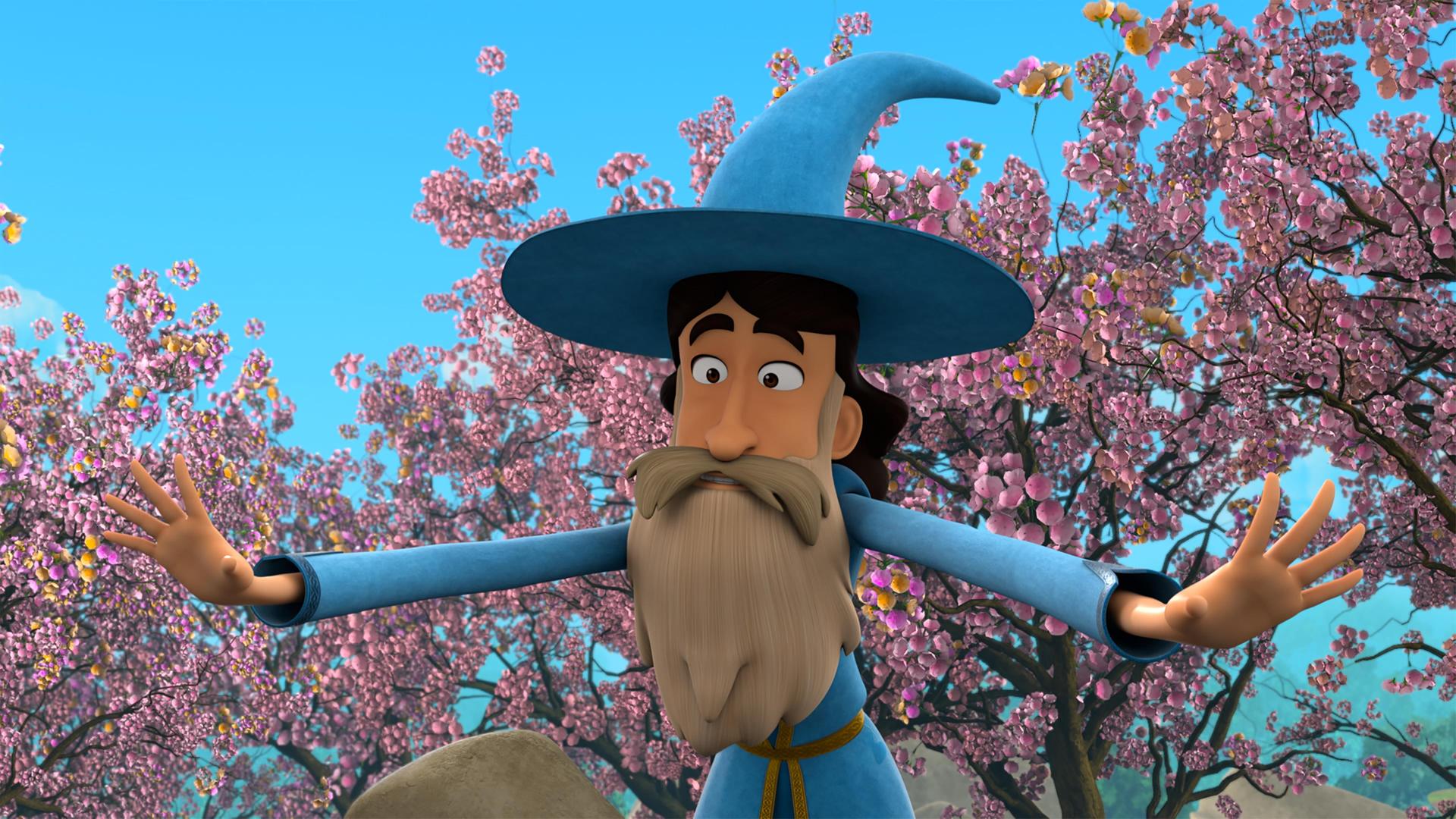 Ein Mann mit dunklem Haar und hellem, langen Bart und Schnurrbart in der blau-goldfarbenen Kleidung von Merlin und dessen Zauberhut, beugt sich mit weit ausgebreiteten Armen zu etwas hinab. Hinter ihm sind Obstbäume, die in voller, rosafarbener Blüte stehen.