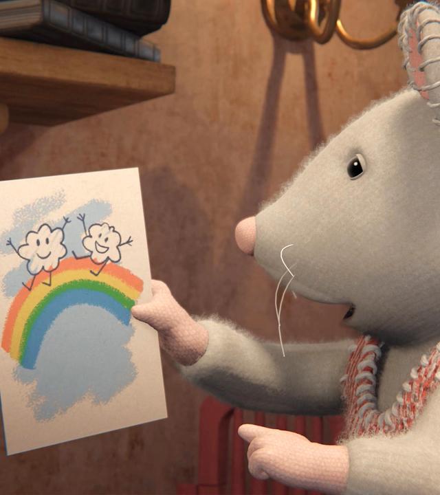 Julia hält ein selbst gemaltes Bild hoch, auf dem ein Regenbogen zu sehen ist, über dem zwei Wolken fröhlich tanzen. Sie schaut das Bild nachdenklich an.