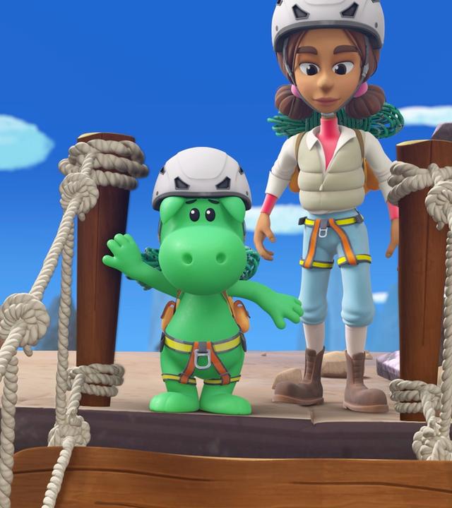 Der kleine Drache Grisu trägt einen weißen Helm und Klettergeschirr. Neben ihm steht Doktorin Natureza ebenfalls mit Helm und Kletterausrüstung. Sie wollen eine Hängebrücke aus Seilen überqueren. Diese ist im Vordergrund des Bildes zu sehen.