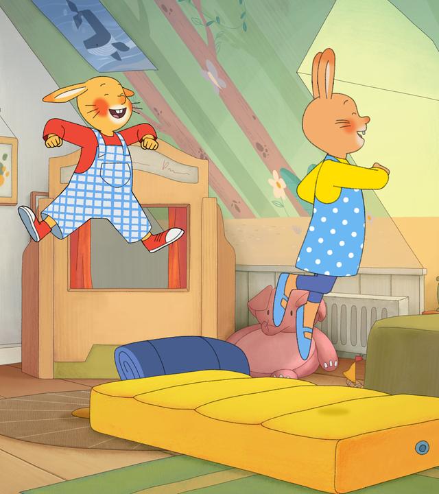 Wir sehen Monikas Kinderzimmer. Auf dem Boden liegt eine gelbe Luftmatratze, auf der Karlchen und Monika herumhüpfen. Bello, der Hund, kommt zur Tür herein. Alle machen lachende Gesichter und freuen sich.