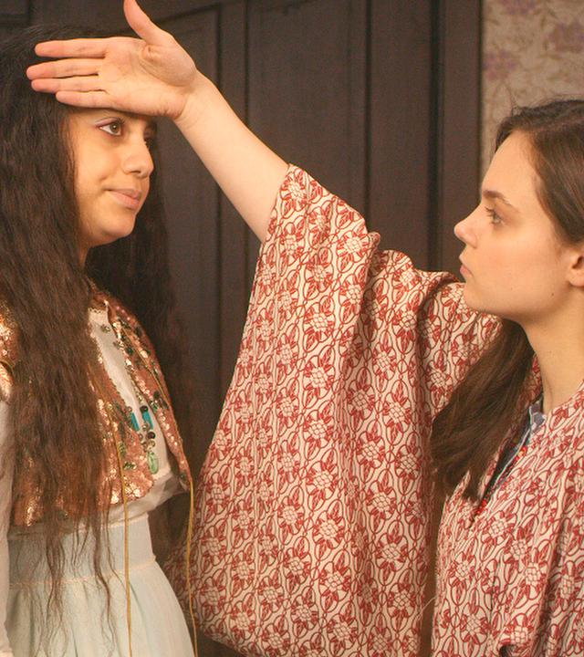Theodosia und Safiya stehen sich gegenüber. Theo fühlt mit der Hand bei Safiya, ob sie Fieber hat.
