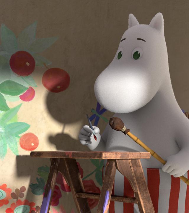 Muminmama steht auf einer Leiter und hält einen Malerpinsel in ihrer Hand. Im Hintergrund ist das von ihr an die Wand gemalte Wandbild zu erkennen: ein Apfelbaum und eine Blumenwiese.