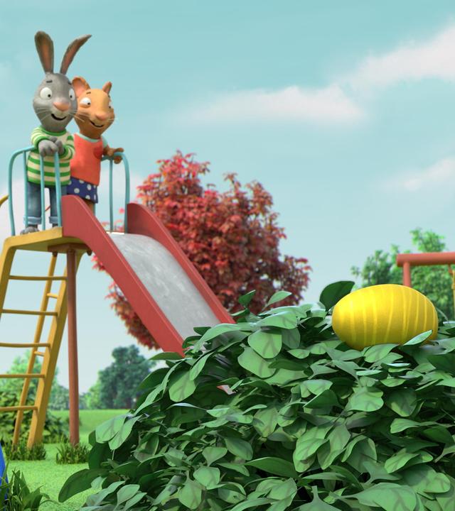 Pip, das Kaninchen und Posy, die Maus stehen gemeinsam auf der Rutsche. Beide schauen aufgeregt zu einem Busch, der sich auf der Wiese befindet. Im Busch liegt ein großes, goldenes Dinoei.
