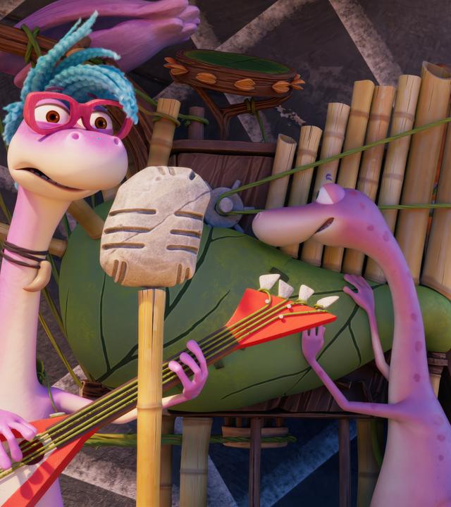 Das Dinosauriermädchen Magma mit der coolen Brille und den blauen Haaren spielt mit einer roten E-Gitarre auf einer Bühne. Vor ihr steht ein steinzeitliches Mikrofon auf einem Stativ. Im Hintergrund steht Minus Drei vor einer merkwürdigen Maschine, die aussieht wie ein Blasebalg mit Orgelpfeifen.