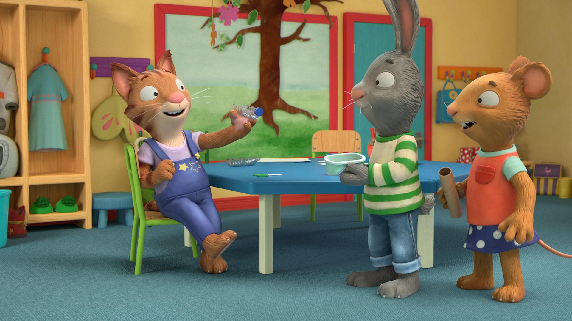 Die Katze Frankie sitzt auf einem Stuhl und hält eine Wasserflasche quer in ihrer linken Hand. Dabei blickt Frankie zu Pip und Posy. Pip, das Kaninchen und Posy, die Maus schauen Frankie begeistert an. Pip hält eine Box in seinen Händen und Posy eine leere Papierrolle. Im Hintergrund hängt ein selbstgebastelter Baum an der Wand.