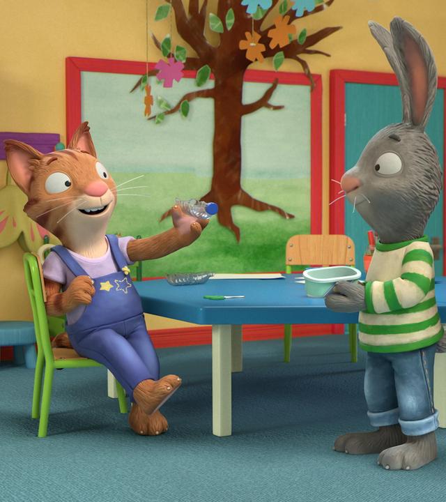 Die Katze Frankie sitzt auf einem Stuhl und hält eine Wasserflasche quer in ihrer linken Hand. Dabei blickt Frankie zu Pip und Posy. Pip, das Kaninchen und Posy, die Maus schauen Frankie begeistert an. Pip hält eine Box in seinen Händen und Posy eine leere Papierrolle. Im Hintergrund hängt ein selbstgebastelter Baum an der Wand.