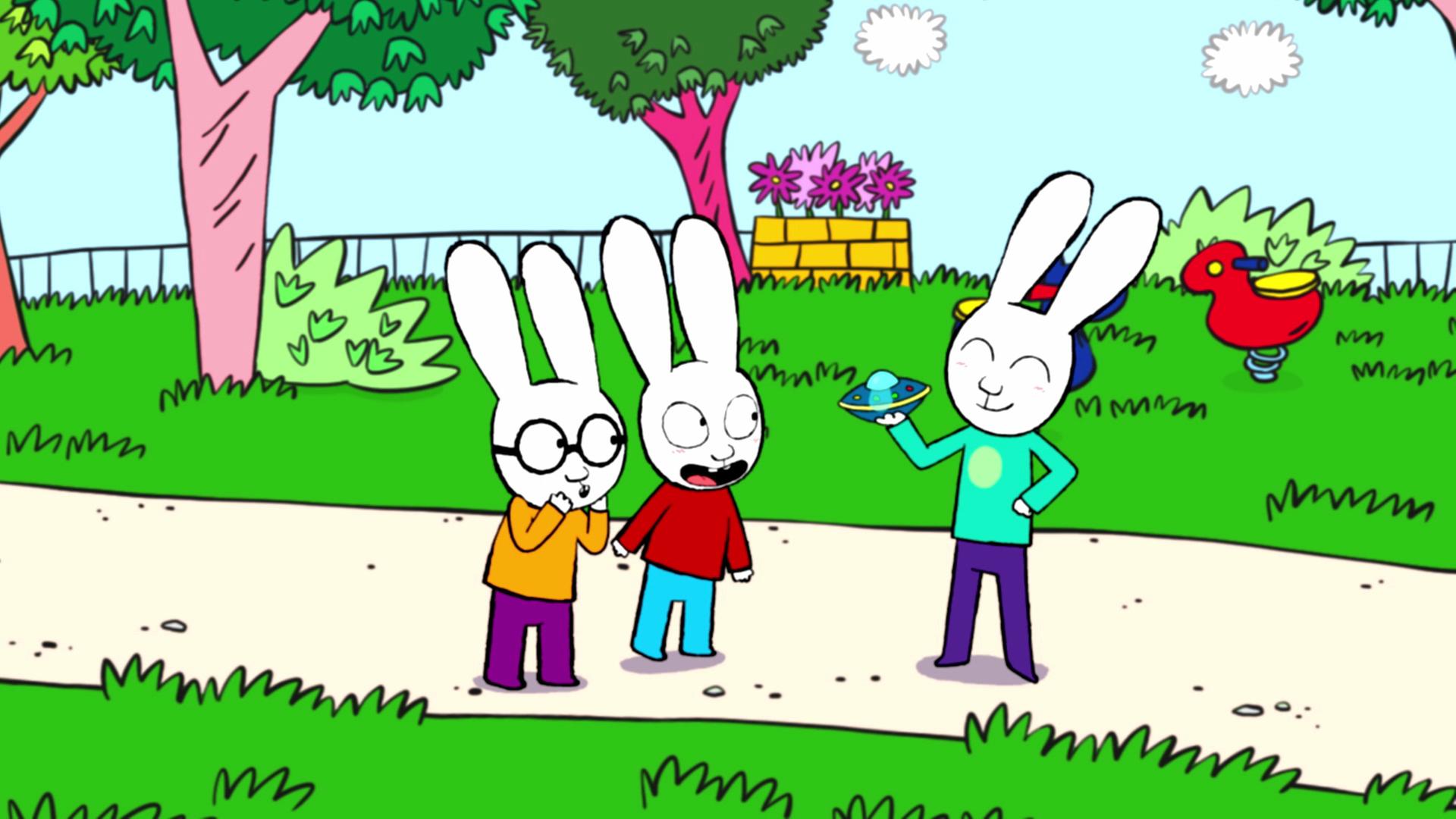 Im Park stehen Ferdinand, Simon und Simons Cousin Benjamin auf dem Gehweg. Benjamin hält ein Spielzeug-Ufo in seiner rechten Hand. Ferdinand schaut bewundernd zu Benjamin. Simon schaut seinen Cousin Benjamin freudig aufgeregt an.