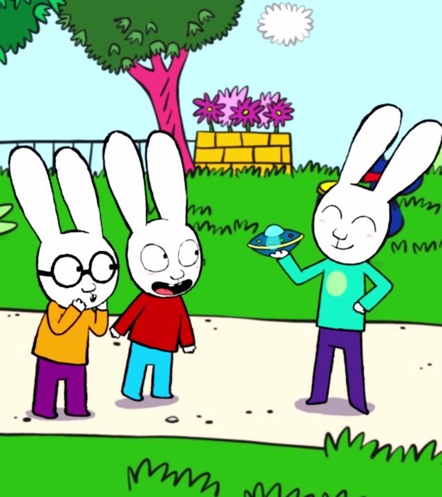 Im Park stehen Ferdinand, Simon und Simons Cousin Benjamin auf dem Gehweg. Benjamin hält ein Spielzeug-Ufo in seiner rechten Hand. Ferdinand schaut bewundernd zu Benjamin. Simon schaut seinen Cousin Benjamin freudig aufgeregt an.