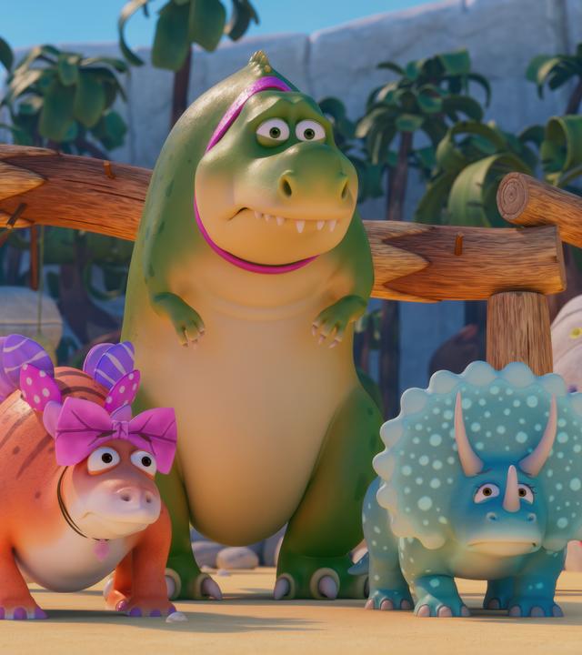 Die Haustier-Dinosaurier Stiggi, Rexie und Topsi stehen auf dem Spielplatz und machen besorgte Gesichter. Rexie ist ein großer, grüner T-Rex mit pink Halsband. Stiggi ist ein orangefarbener Stegosaurus mit rosa und pink Schleifen und Topsi ist ein türkisfarbener Triceratops.