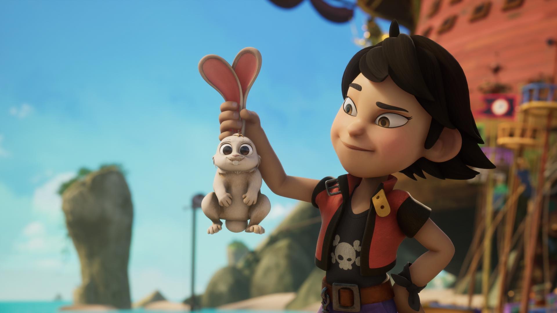 Draußen am Strand steht Zoe. Sie hat ihren linken Arm in die Hüfte gestemmt und in der rechten Hand hält sie ein niedliches Kaninchen an beiden Ohren hoch und schaut es freundlich an.