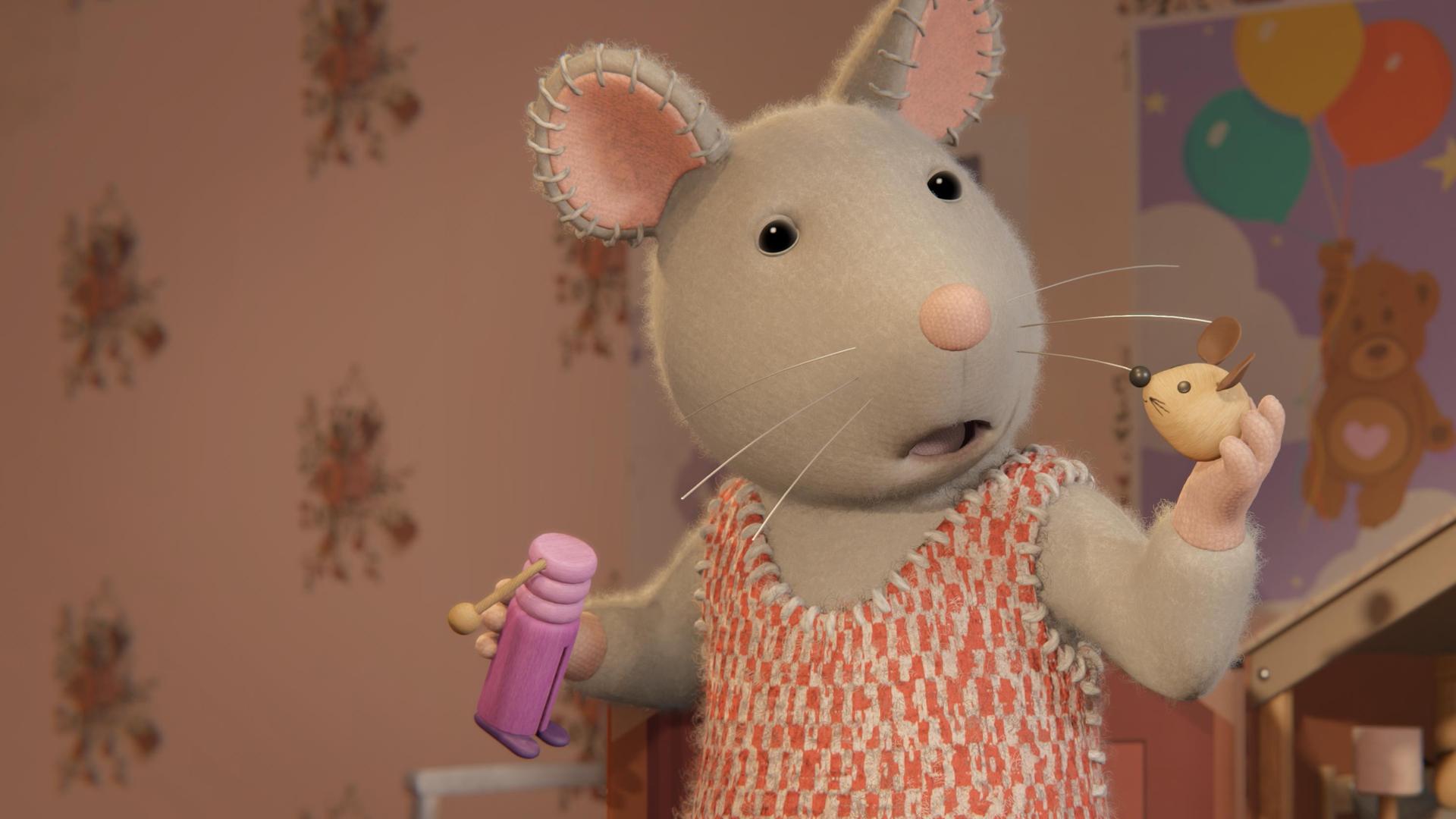 Julia steht in einem Kinderzimmer vor einem Puppen-Mäusehaus. Sie hält in der rechten Hand einen Puppenkörper, in der linken Hand den Kopf der Mauspuppe und schaut erschrocken zu dem Kopf.