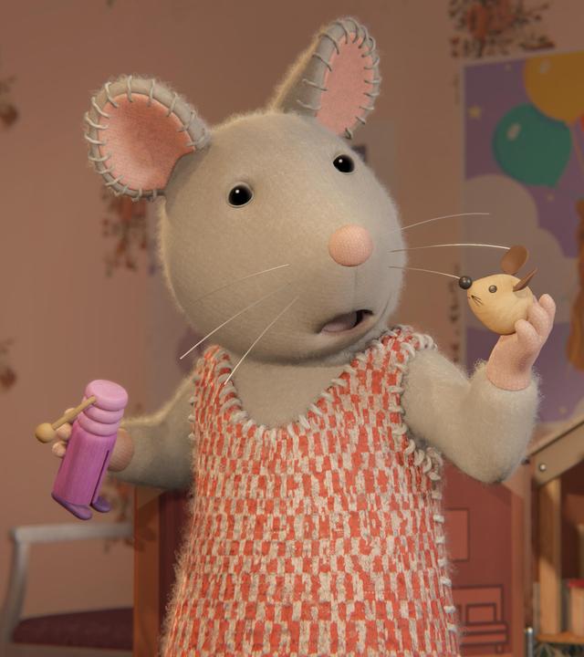 Julia steht in einem Kinderzimmer vor einem Puppen-Mäusehaus. Sie hält in der rechten Hand einen Puppenkörper, in der linken Hand den Kopf der Mauspuppe und schaut erschrocken zu dem Kopf.