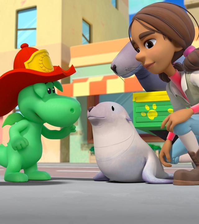 Grisu, Stella und Doktorin Natureza stehen um ein kleines Seelöwenbaby herum. Aber nicht am Strand sondern mitten in Drachenstadt.