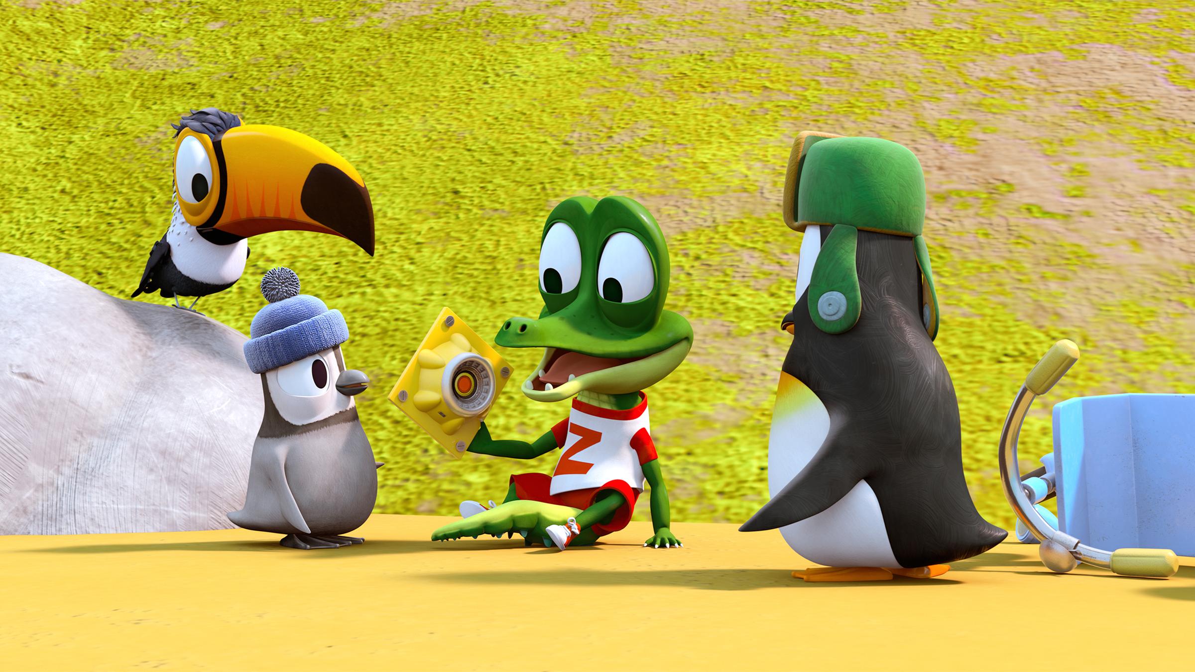 Krokodil Zacki (Mitte) hält freudestrahlend ein Ersatzteil für die Bahn in seiner Hand. Die Pinguine Kurti (links) und Jonathan (rechts) und der Tukan Toni (links) schauen Zacki dabei interessiert zu.