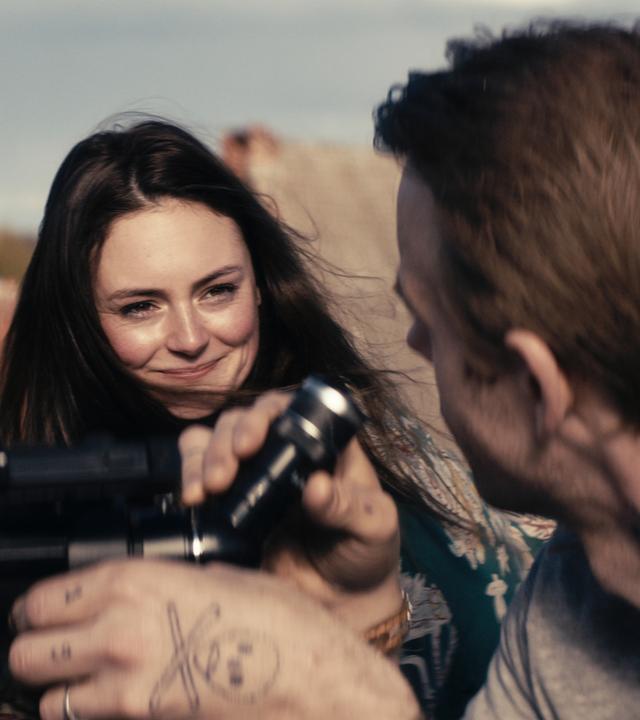 Ella (Lea van Acken) hält eine Zigarette in der Hand. Sie sitzt neben Jan (Mads Hjulmand), der etwas durch ein Fernrohr beobachtet.