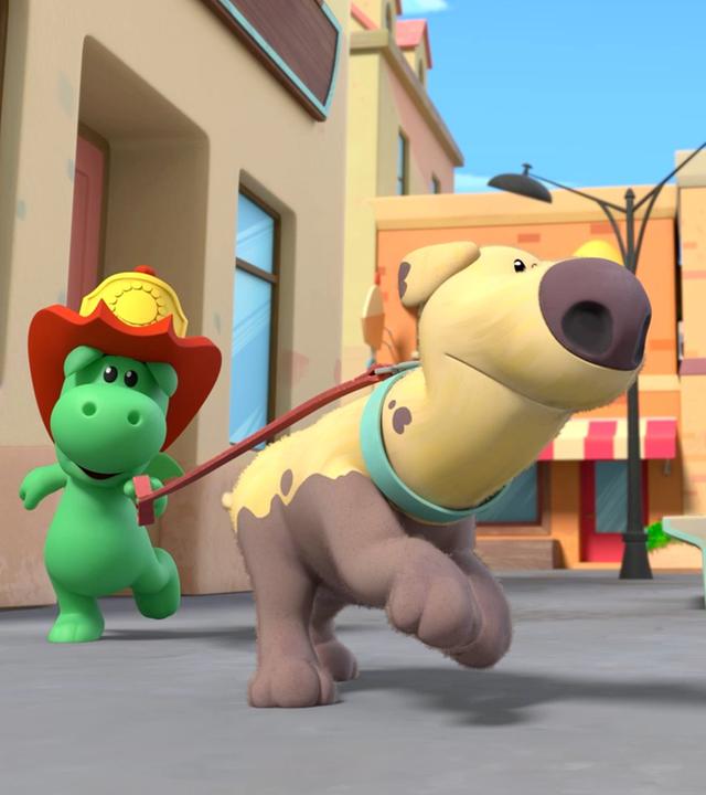 Grisu, der kleine grüne Drache mit dem roten Feuerwehrhelm, hat den Hund Dinki an der Leine. Beide rennen sie durch eine Straße von Drachenstadt. Etwas abseits beobachtet sie dabei Stella.