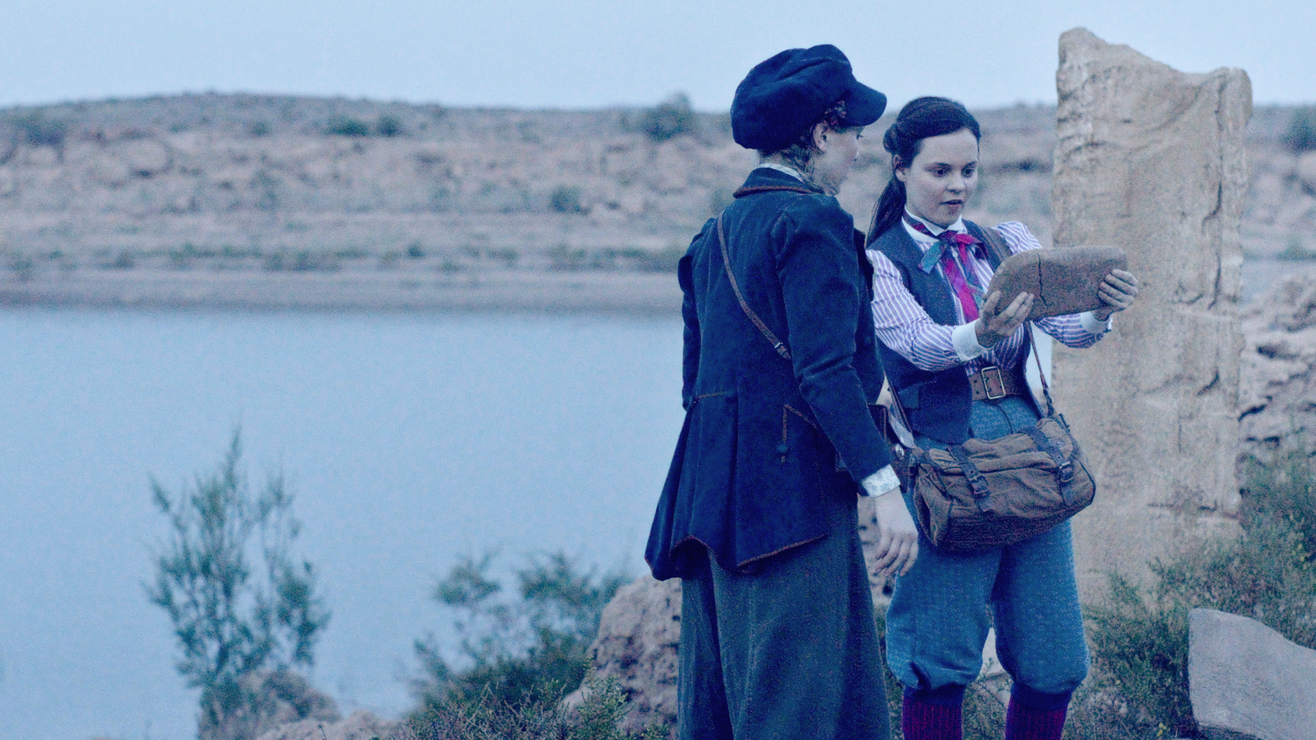 Maya und Theo finden in einer ägyptischen Ruine einen Hinweis auf einem Stein. Sie stehen nebeneinander und Theo hält den Stein mit beiden Händen.