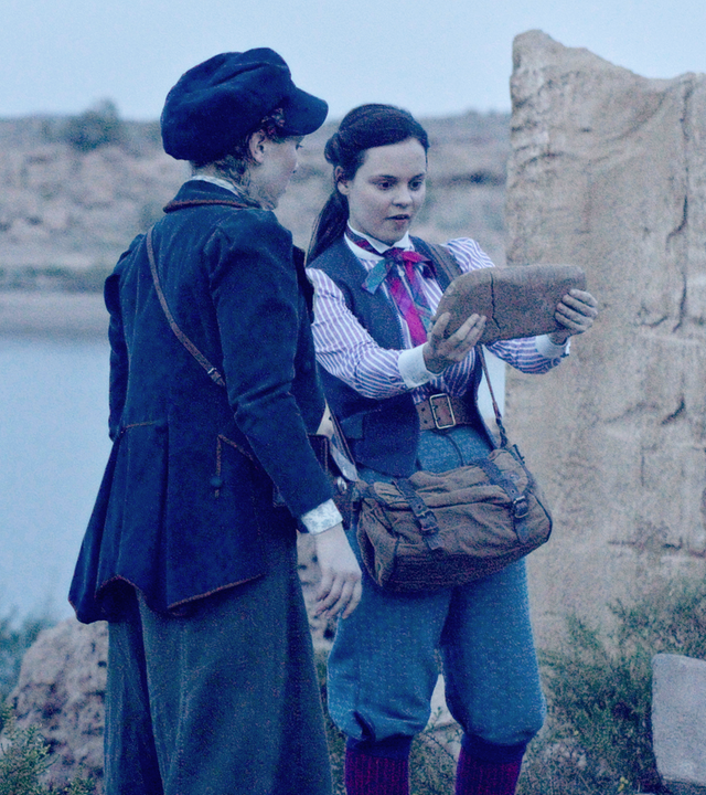 Maya und Theo finden in einer ägyptischen Ruine einen Hinweis auf einem Stein. Sie stehen nebeneinander und Theo hält den Stein mit beiden Händen.