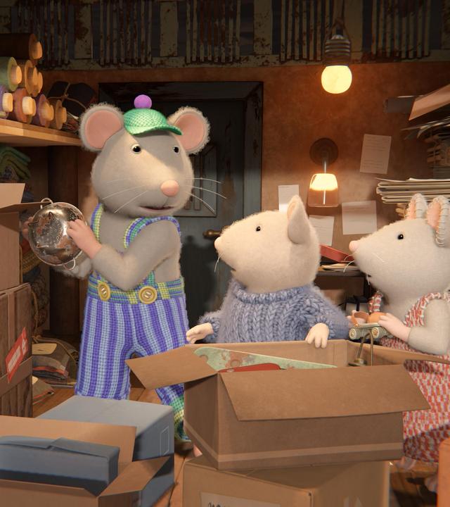 Sam und Julia stehen vor einem großen, aufgeklappten Karton und schauen von der Seite auf Onkel Lumpi, der im Keller ein Sieb in eine Kiste räumt.