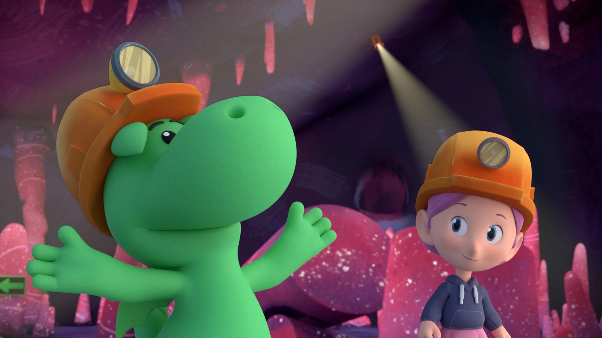 Grisu, der kleine Drache, und seine Freundin Stella stehen in einer Höhle mit rosafarbenen Steinen. Sie tragen Helme mit Stirnlampen. Grisu macht mit den Händen eine ausladenden Geste.