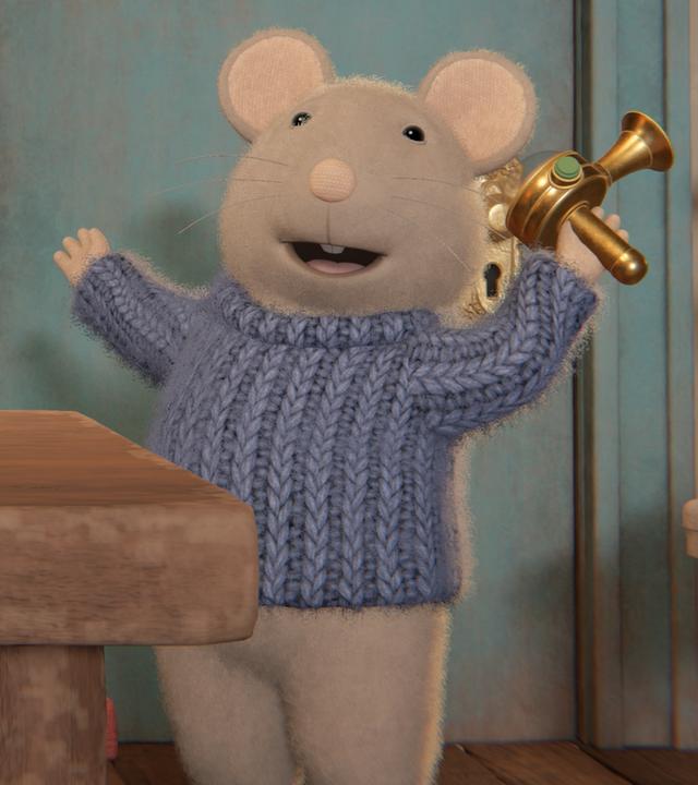 Julia sitzt an einem Tisch im Wohnzimmer vor einem Bücherregal und schaut zu Sam. Der steht vor ihr und hat ein Gerät aus Metall in der linken Hand.