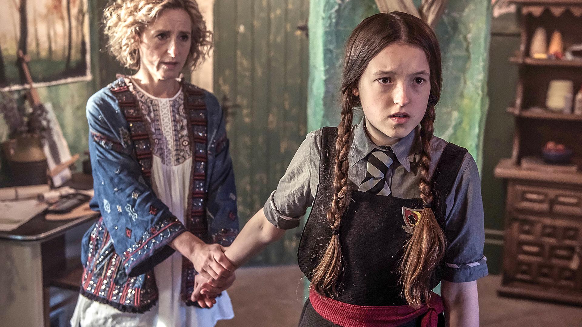 Mildred (rechts) und ihre Mutter Julie (links) stehen in einem Klassenraum. Julie hat ihre Tochter am Arm gepackt, um zu verhindern, dass sie geht.