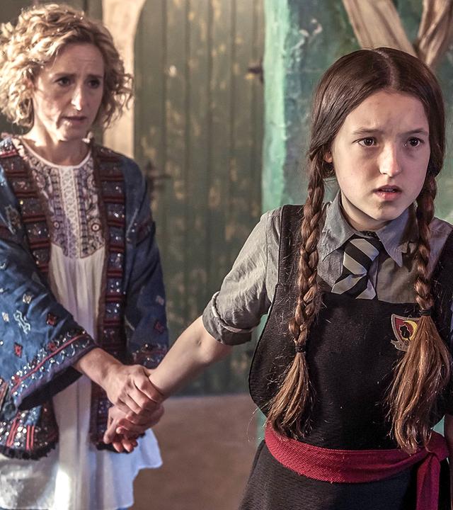 Mildred und ihre Mutter Julie stehen in einem Klassenraum. Julie hat ihre Tochter am Arm gepackt, um zu verhindern, dass sie geht.