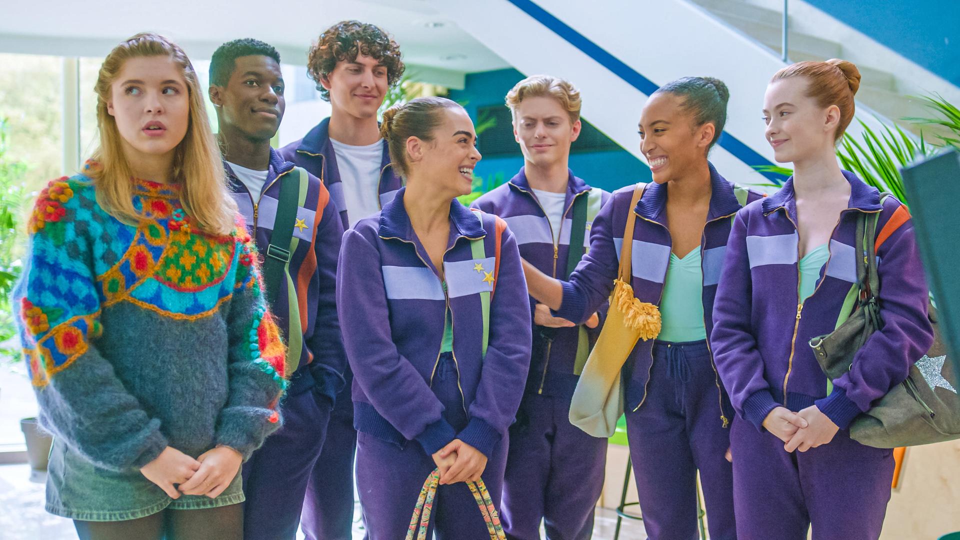 In ihren lilafarbenen Trainingsanzügen steht die Tanzgruppe beisammen und freut sich über Simone, die in der Mitte steht, und Cece freudestrahlend anblickt. Jack, Benoit, Finn und Mia freuen sich mit ihr. Nur Jade steht am Rand der Gruppe und blickt genervt in die andere Richtung. Sie trägt kurze Jeans und einen bunten Pullover.