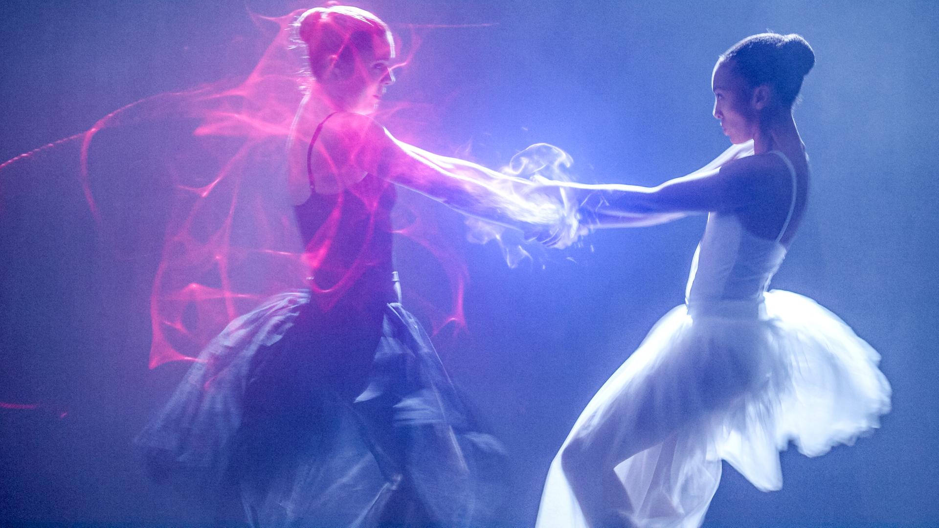 Jade und Cece tanzen miteinander auf der Bühne. Jade trägt ein schwarzes, Cece ein weißes Ballettkleid. Sie halten sich an den Händen und es kommt zu magischen Funken.