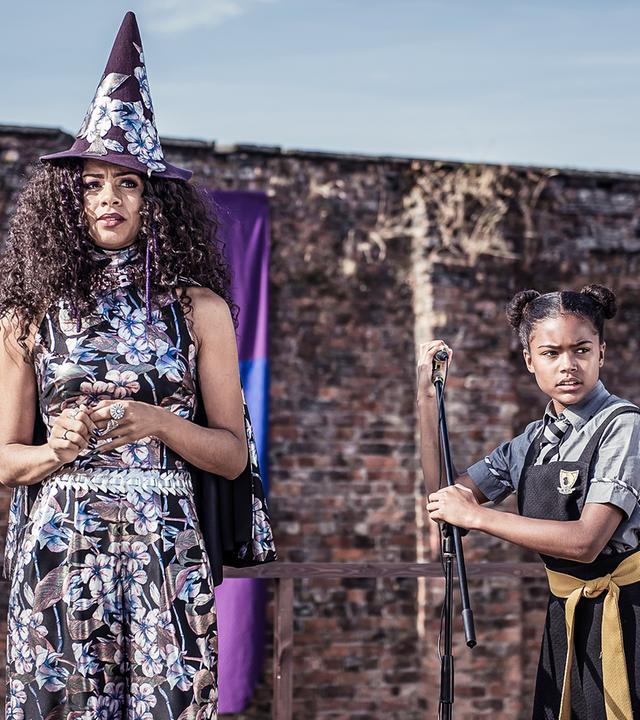 Edith und ihre Mutter stehen auf einem Podest und schauen in die Ferne. Edith hält einen Mikrofon-Ständer.