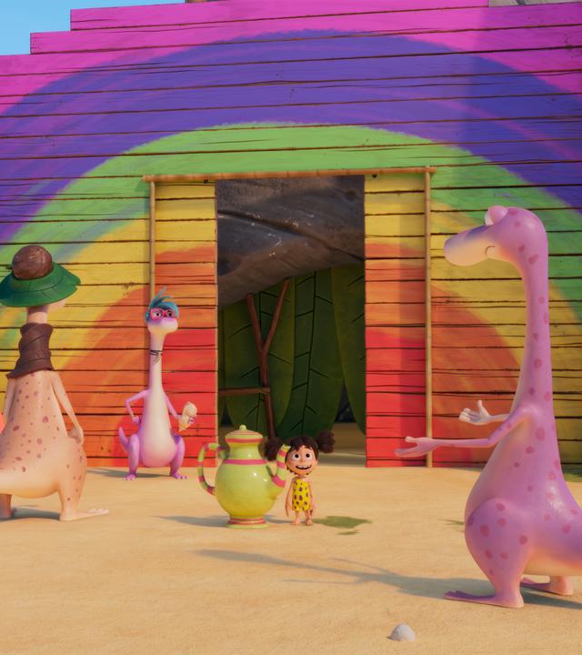 Wir sehen im Hintergrund eine Regenbogenfarbene Bretterwand, in die eine Schiebetür eingelassen ist. Vor der Tür hat sich eine Dinosaurier-Schlange gebildet. Lucy steht ebenfalls davor, sie hat eine riesige Tee-Kanne neben sich und strahlt Minus Drei an, der vor ihr steht und scheinbar nicht glauben kann, was er da gerade sieht.