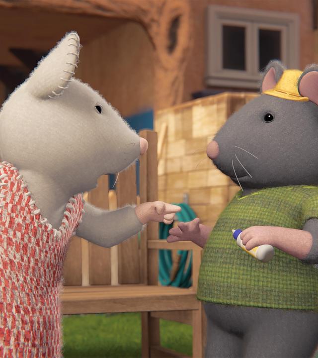 Julia steht vor Tonio, spricht zu ihm und deutet mit ihrem linken Zeigefinger auf ihn. Die beiden stehen im Garten vor einer Parkbank. Im Hintergrund ist die Fassade des Mäusehauses zu sehen.