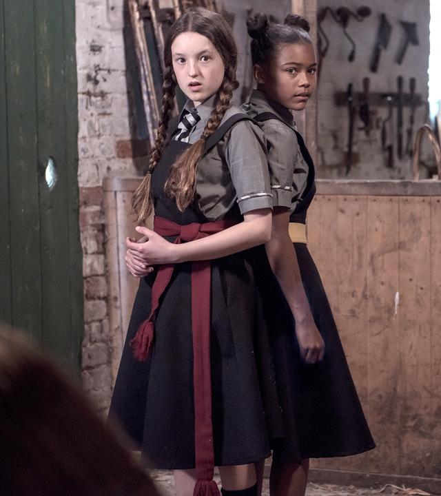 Mildred und Edith stehen Rücken an Rücken in einer Besenkammer. Sie schauen bestürzt auf etwas.