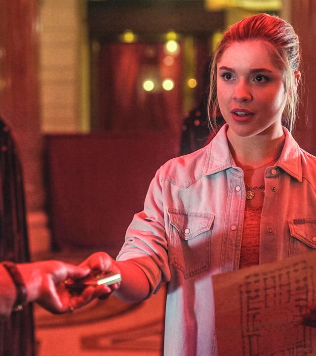 Jade hält einen Lageplan in ihrer linken Hand. Sie reicht ihre Mutter Zoe, die im Bild nur im Anschnitt und von hinten zu sehen ist, einen Gegenstand. Im Hintergrund stehen Männer des Mystik-Zirkels. Sie tragen Umhänge mit Kapuzen, die sie über den Kopf gezogen haben.