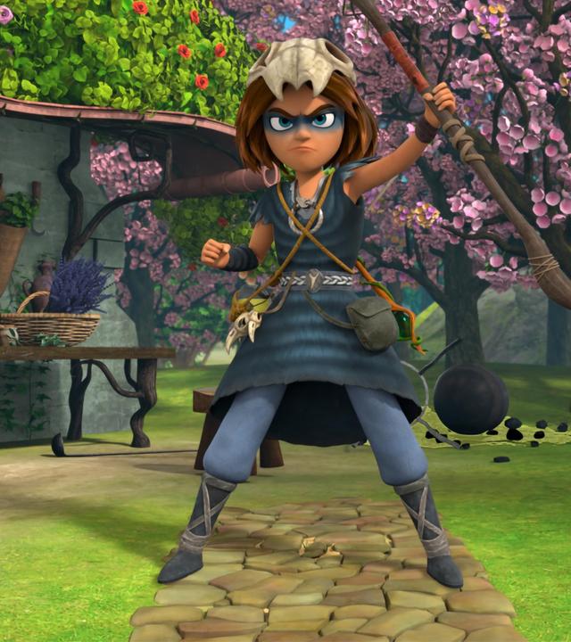 Auf einem gepflasterten Weg im erblühten Garten vor Katells Haus steht der Schamanenjunge Stig. Seinen Druidenstab hält er mutig und stolz nach oben und sein Blick ist entschlossen.