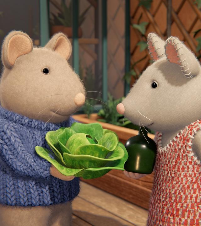 Sam und Julia stehen auf der Terrasse zwischen Hochbeeten mit Salatköpfen. Sam hält einen Salatkopf in den Händen und zeigt ihn Julia.