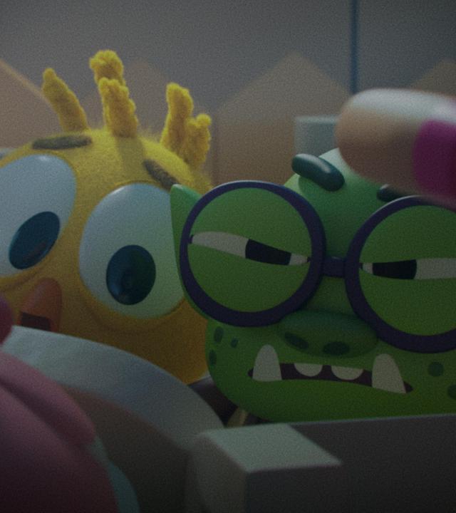 Das Küken Karla und Troll Oggi blicken angespannt und verängstigt nach vorne. Ihre Körper sind nicht vollständig sichtbar, da sie sich hinter einem Zaun verbarrikadiert haben. Das Einhorn-Schwein Ophelia steht auf der anderen Seite des Zauns und versucht zu ihnen vorzudringen.