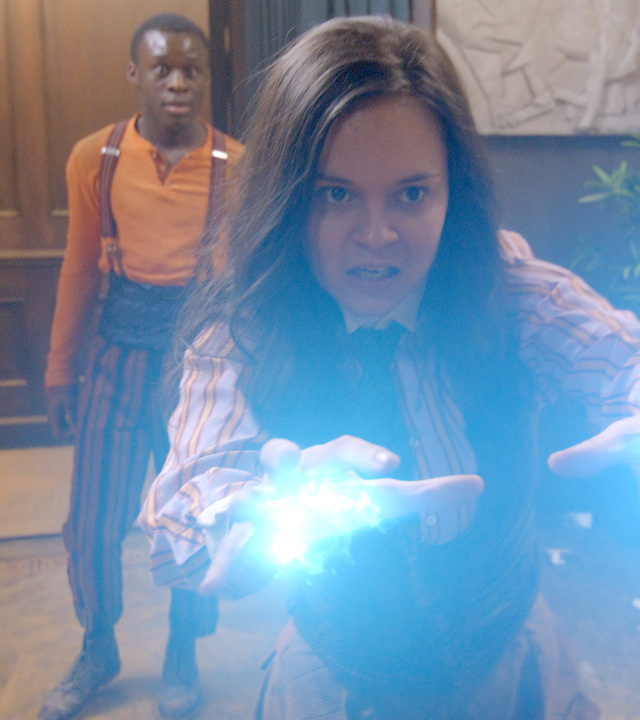 Will steht überrascht hinter Theo, die mit ausgestreckten Händen ihre Magie in Form von blauen Blitzen ihrem Feind entgegenschleudert.