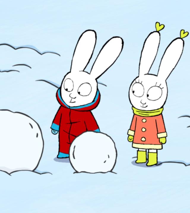 Simon und Lou stehen vor zwei großen Schneebällen. Es ist ein verschneiter Tag und die beiden haben ihre Schneeanzüge an.