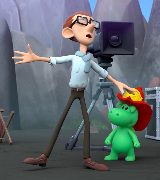 Grisu mit seinem roten Feuerwehrhelm, Stella und der Filmregisseur Ratatino stehen an einem Filmset. Im Hintergrund steht eine große Filmkamera auf einem Stativ. Ratatino macht eine verzweifelte Geste.