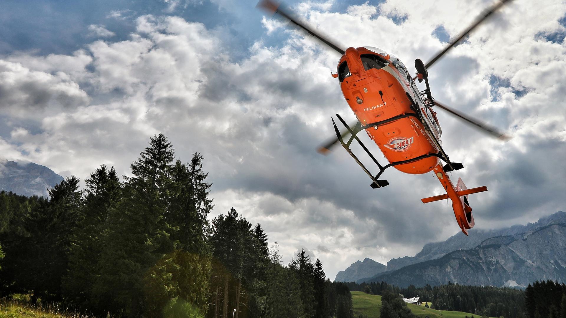Von unten gesehen landet ein orangefarbener Hubschrauber der südtiroler Flugrettung in alpiner Landschaft