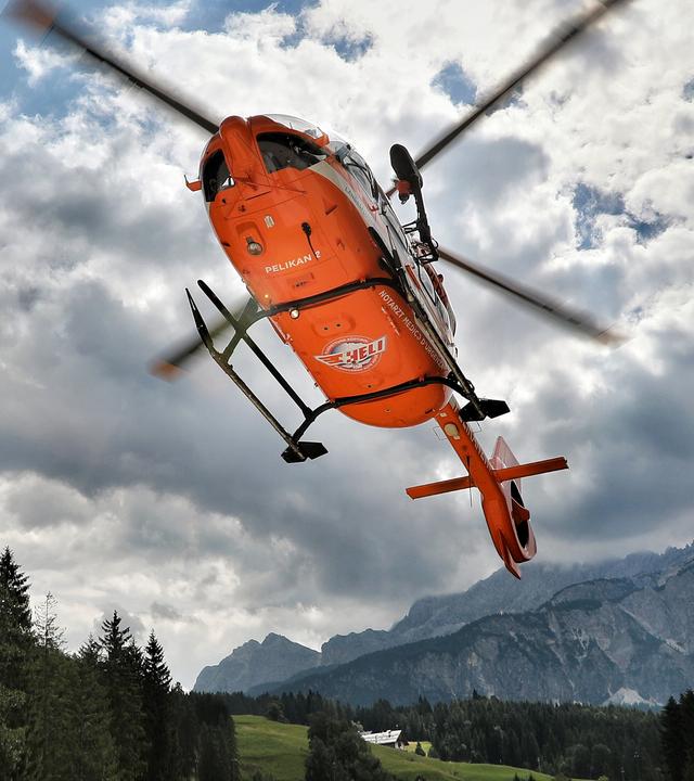 Von unten gesehen landet ein orangefarbener Hubschrauber der südtiroler Flugrettung in alpiner Landschaft