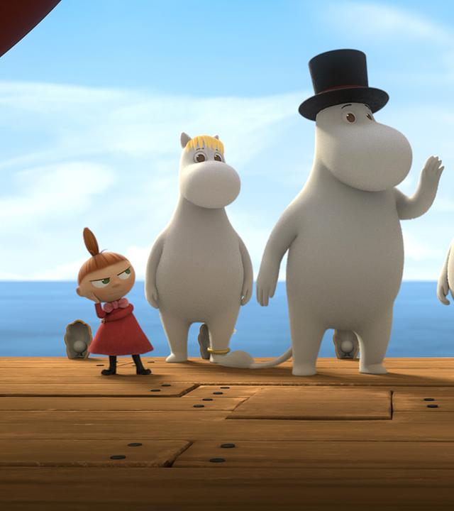 Die ganze Muminfamilie steht auf einer Theaterbühne, hinter ihnen ist Wasser und ein hellblauer Himmel zu sehen.